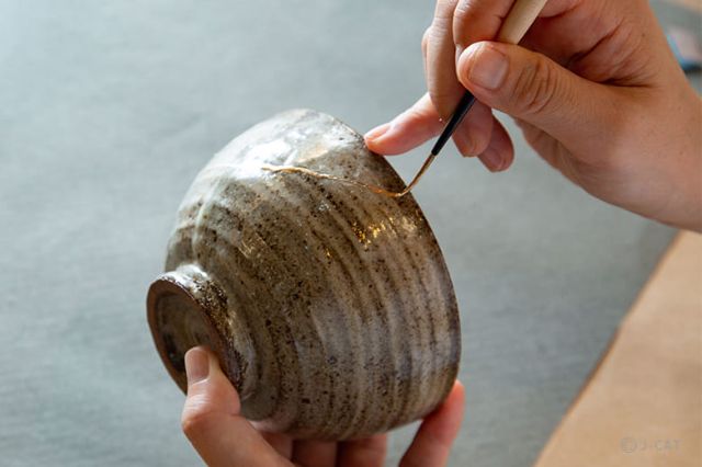 Artisan applying gold lacquer to repair a ceramic bowl during a traditional kintsugi workshop in Japan.