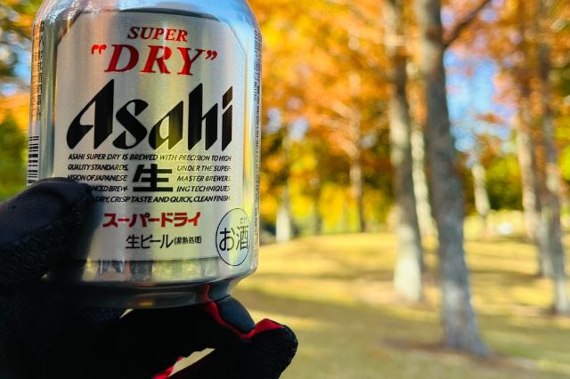Can of Asahi Super Dry held on a golf course with autumn trees in Japan