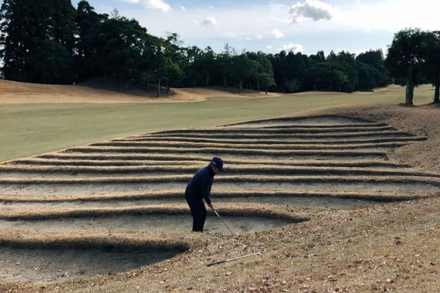 Golfer hitting a shot from a deep layered bunker on a Japanese golf course