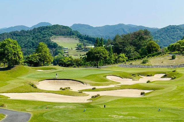 Wide view of a Japanese golf course with sand bunkers and green mountains in the background